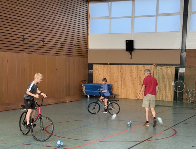 2 Radball spielende Kinder plus Übungsleiter